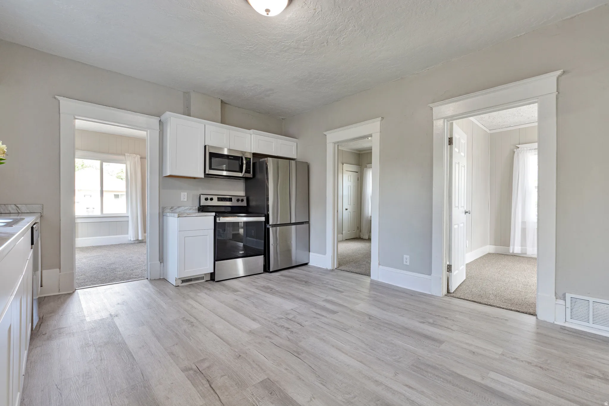 Open-concept kitchen featuring light wood-finish flooring, white cabinetry, stainless steel appliances, and a light-toned countertop