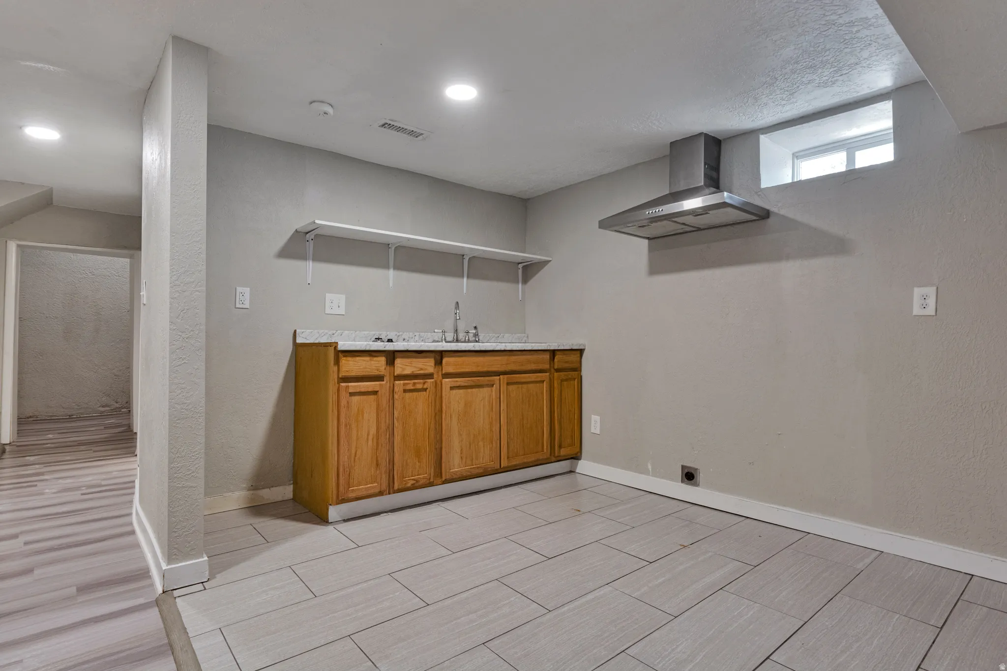 Kitchenette featuring wood cabinetry, a sink with a stainless steel faucet, and a wall-mounted stainless steel range hood