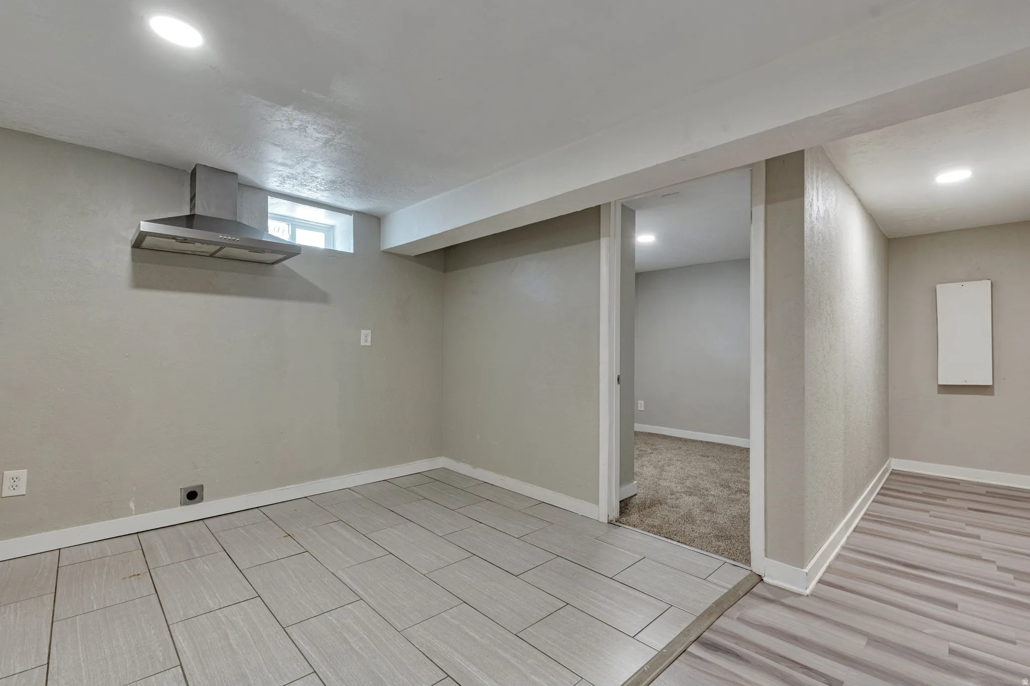 Versatile space featuring light-toned tile flooring and a stainless steel range hood