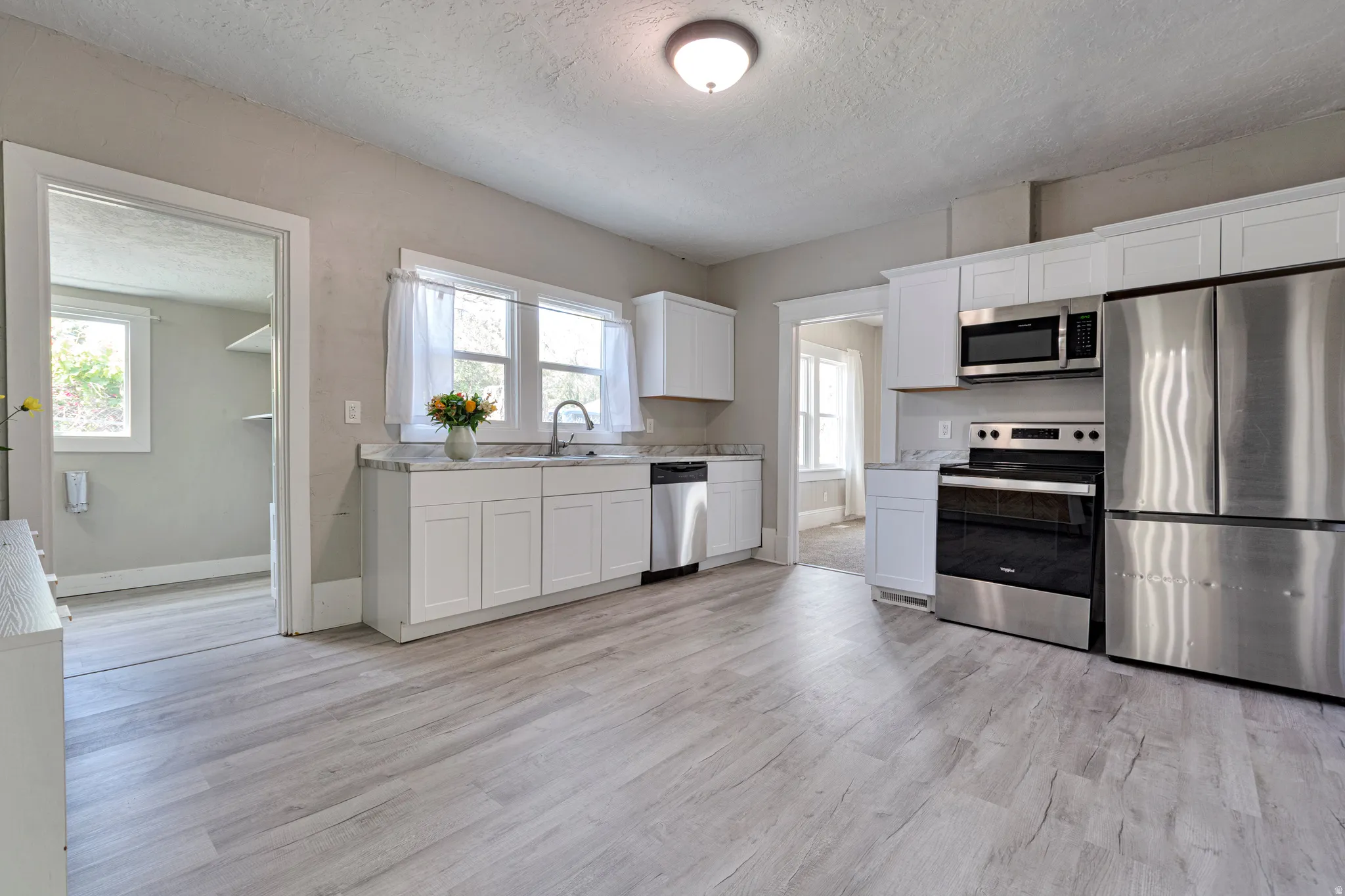 Kitchen featuring wood-finish flooring, white cabinetry, stainless steel appliances, and a double window above the sink