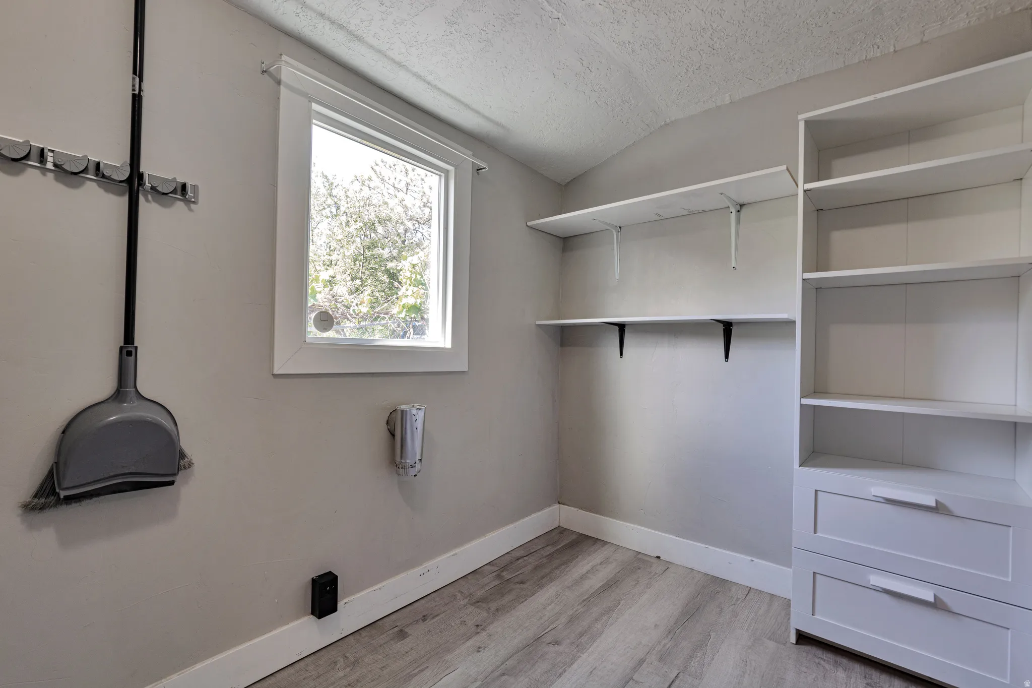 Room with wood-finish flooring, built-in shelving, and a single window