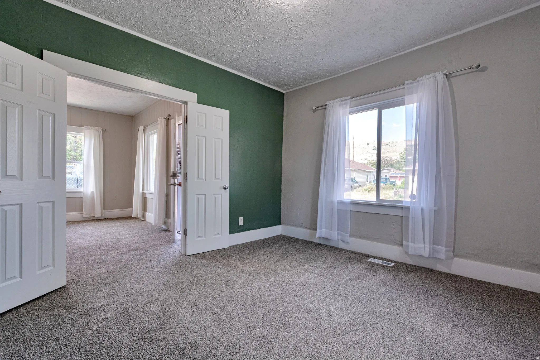 Spacious interior featuring a neutral carpet flooring, a large window with natural light, a contrasting accent wall, white trim, and white paneled doors