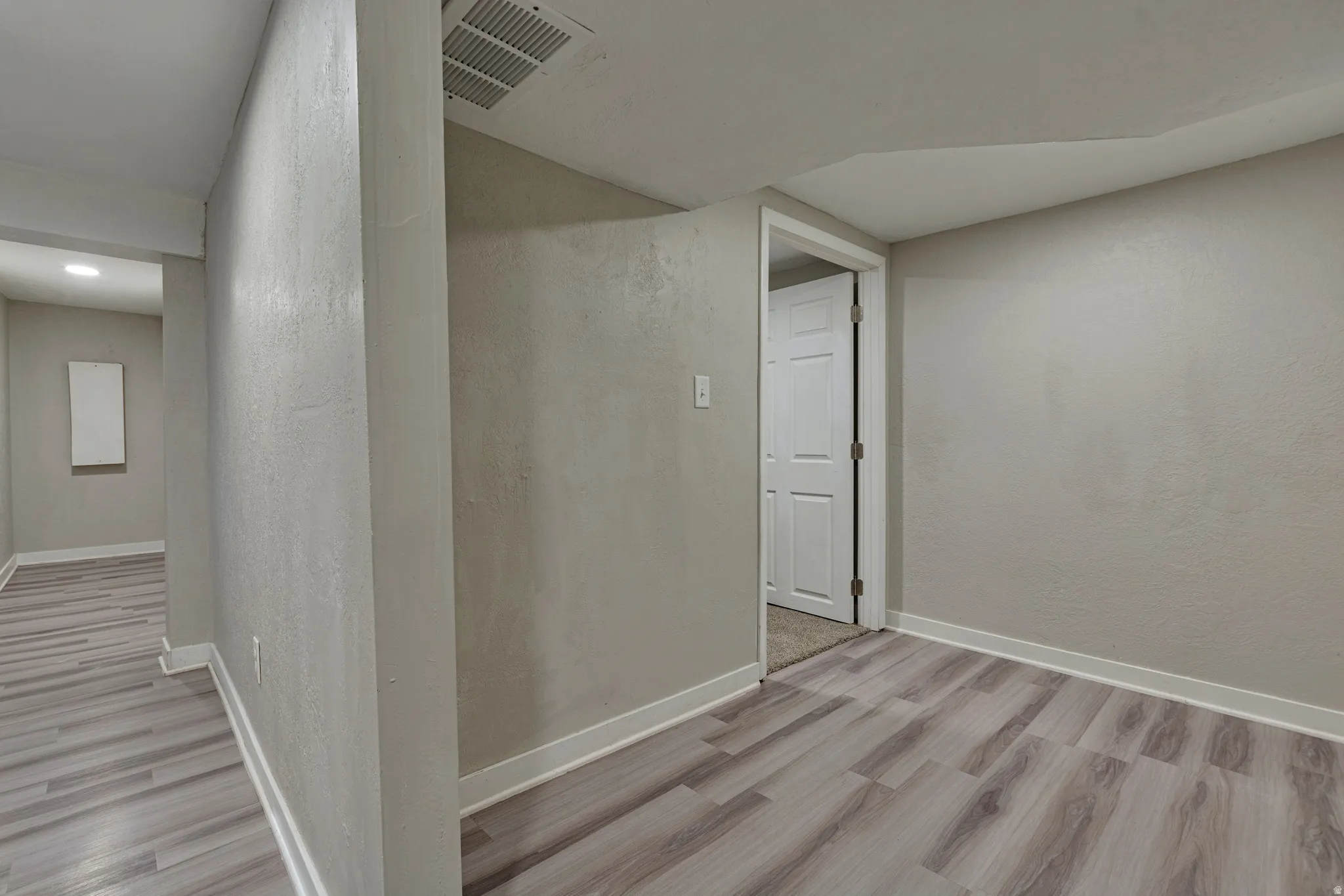Interior space featuring light wood-finish flooring, light gray walls, white baseboards, and a white paneled door