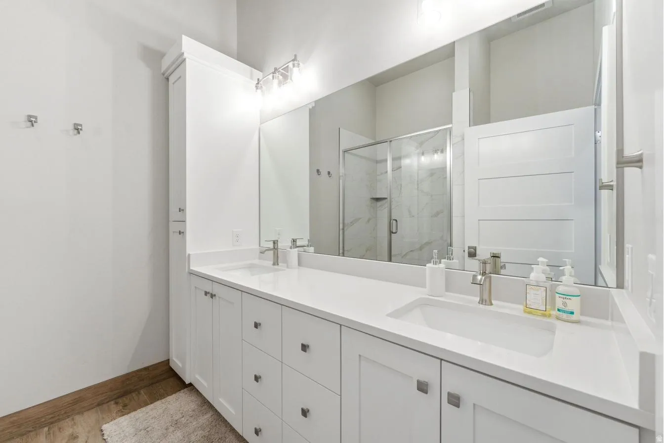 Bathroom featuring a dual vanity with white cabinetry, integrated sinks, and brushed nickel hardware