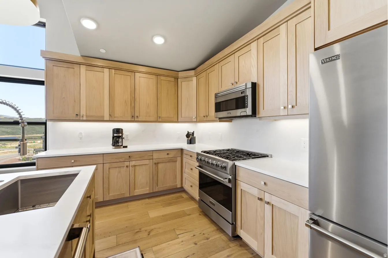 Kitchen featuring light wood-finish cabinetry, white countertops, stainless steel appliances, and wood-finish flooring