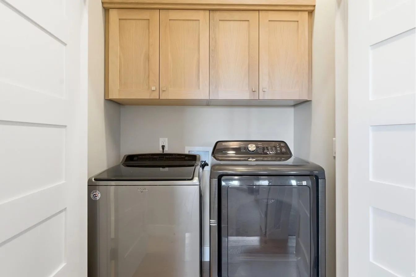 Dedicated laundry area featuring light wood cabinetry, white shaker-style doors, light gray wall paint, and a built-in electrical outlet