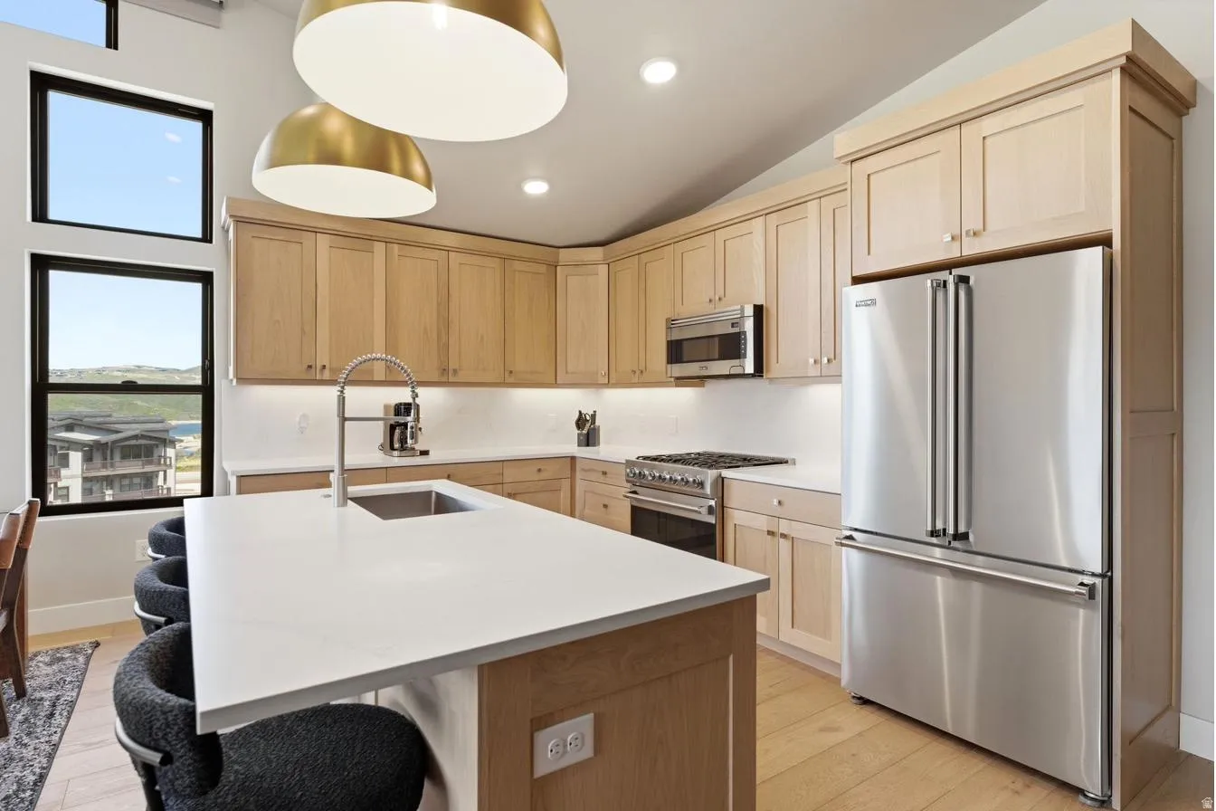 Modern kitchen featuring light wood cabinetry, a large kitchen island with a single-basin sink and gooseneck faucet, stainless steel appliances, and light-toned countertops