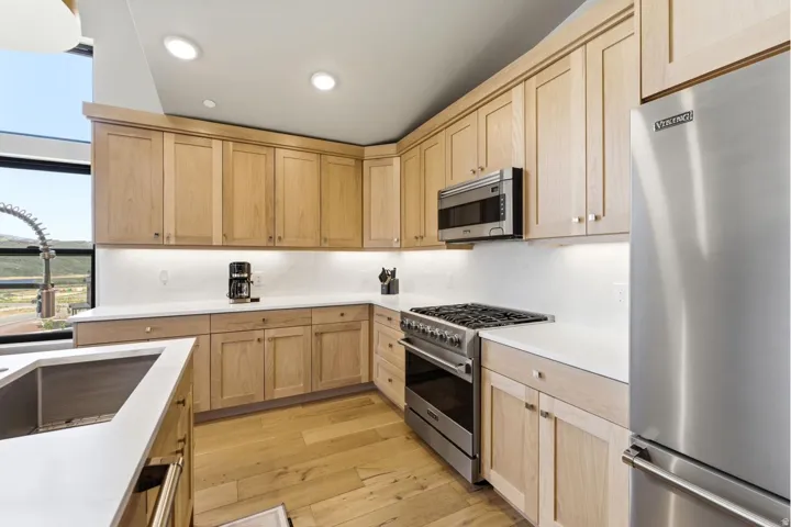 Kitchen featuring light wood-finish cabinetry, white countertops, stainless steel appliances, and wood-finish flooring