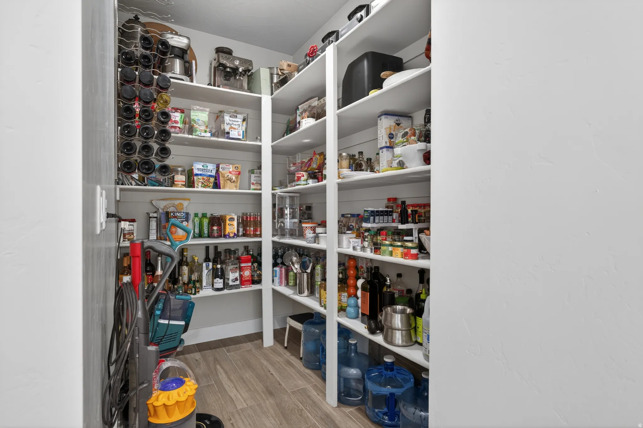 Walk-in pantry featuring extensive built-in shelving, wood-finish flooring, and integrated wine storage