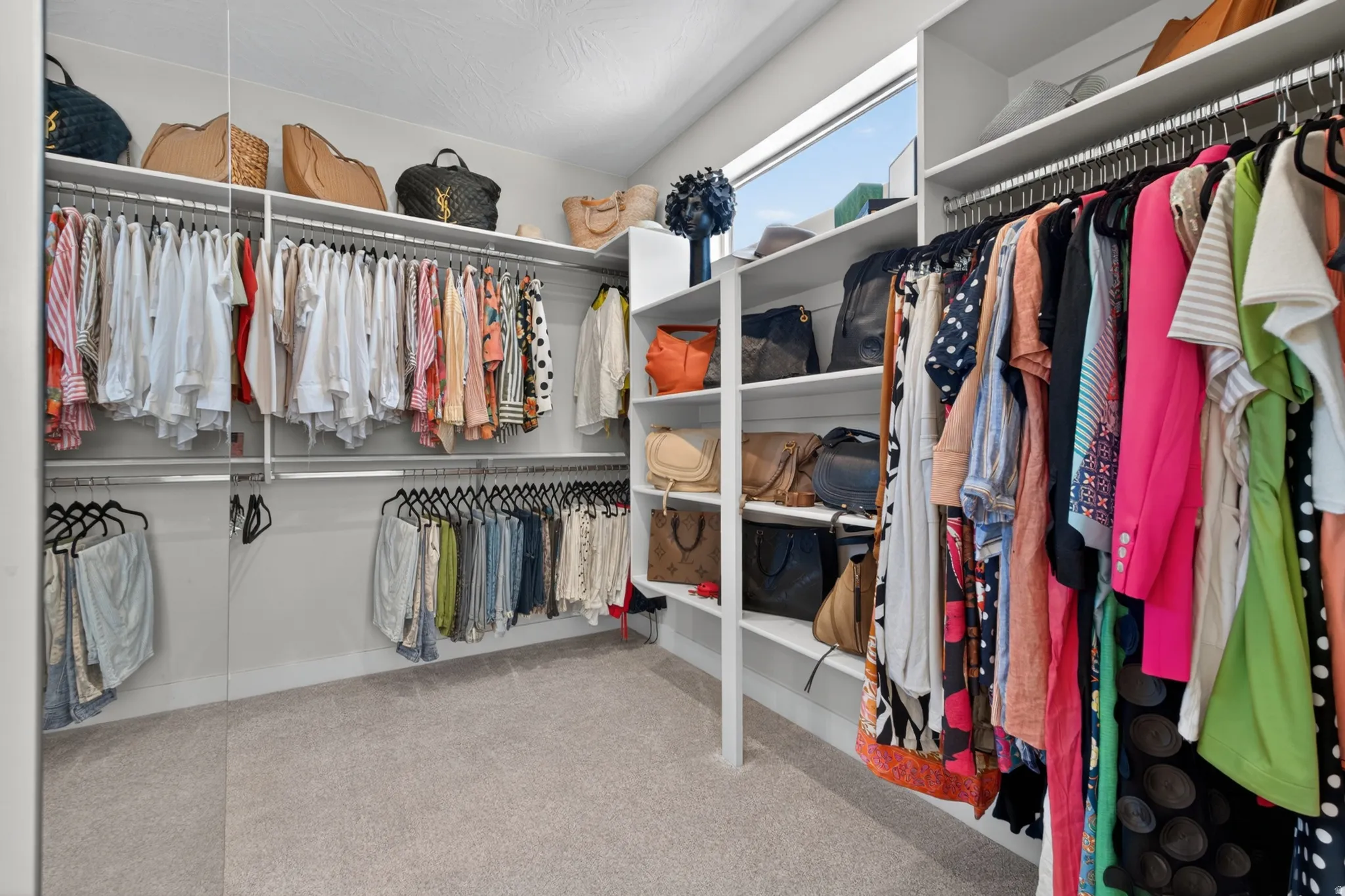 Expansive walk-in closet featuring extensive built-in shelving, multiple hanging rods, and light-toned carpeting