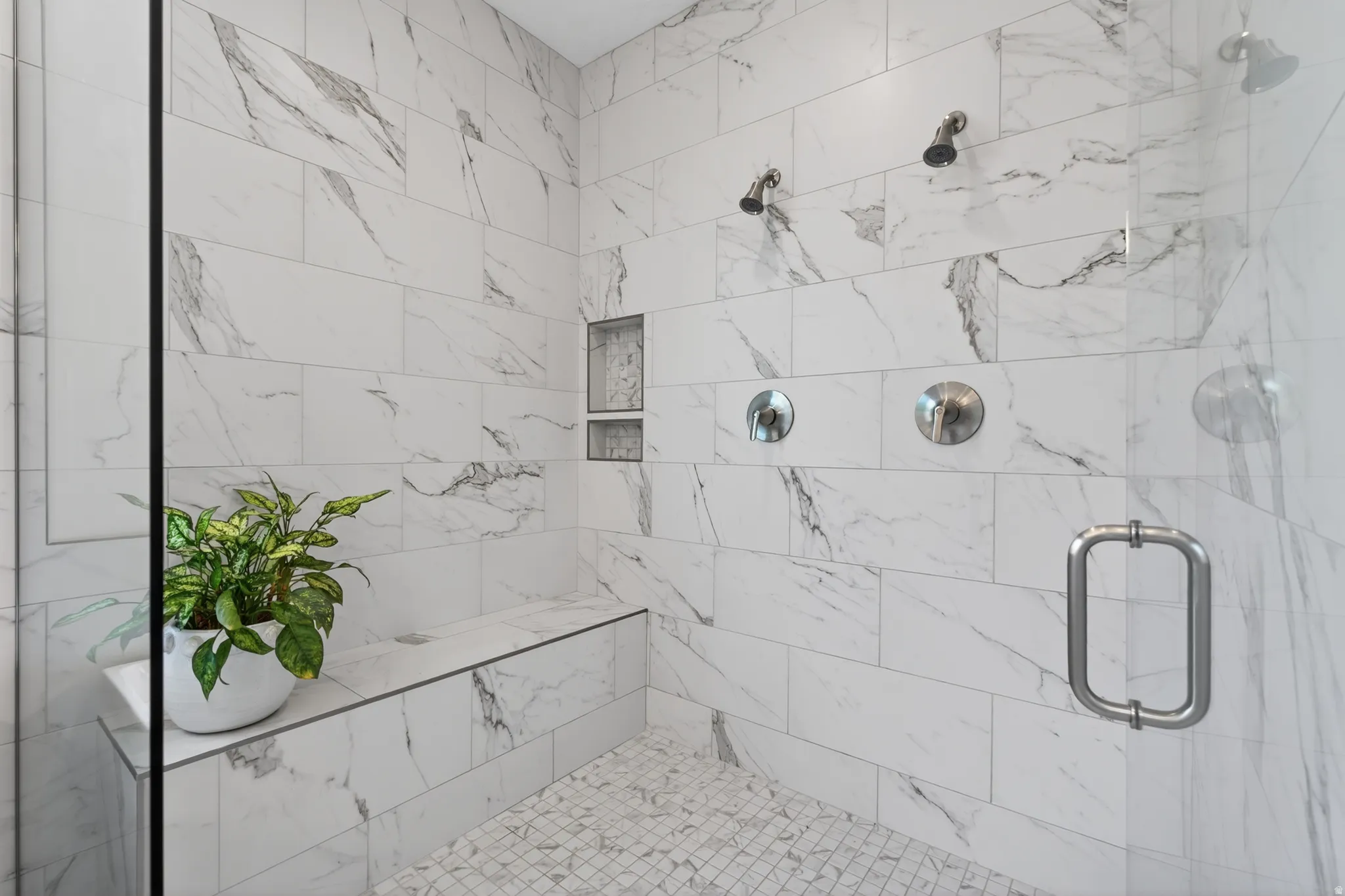 Spacious walk-in shower featuring large format tile walls, a built-in bench, and a mosaic tile floor