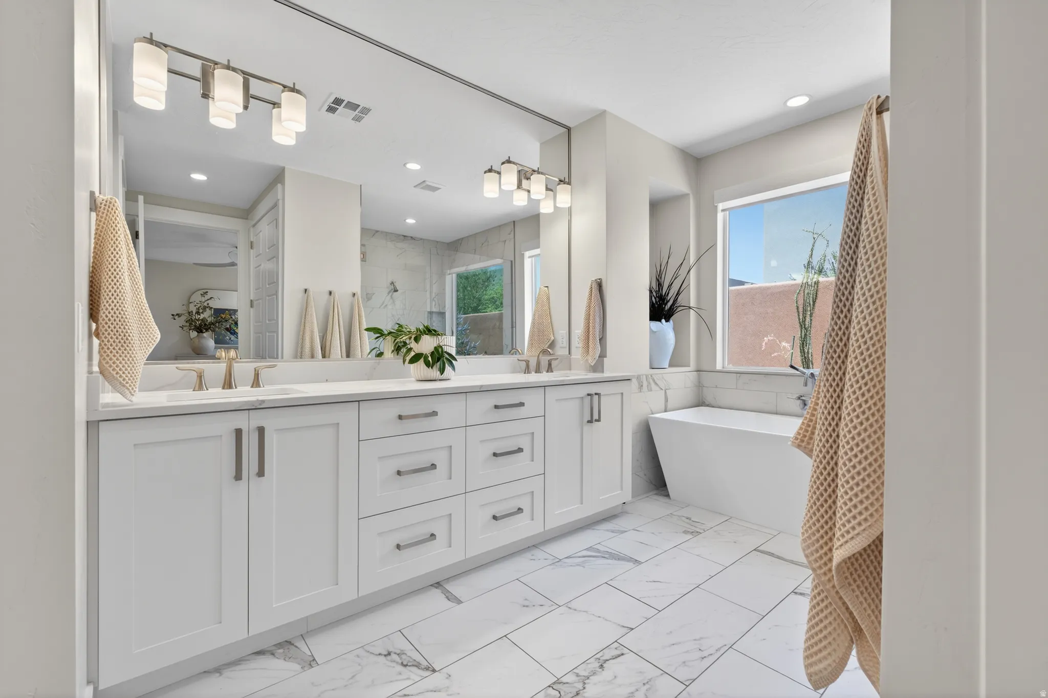 Contemporary bathroom featuring a dual vanity with white shaker cabinetry and brushed nickel hardware, a rectangular undermount sink, and a large mirror with integrated lighting