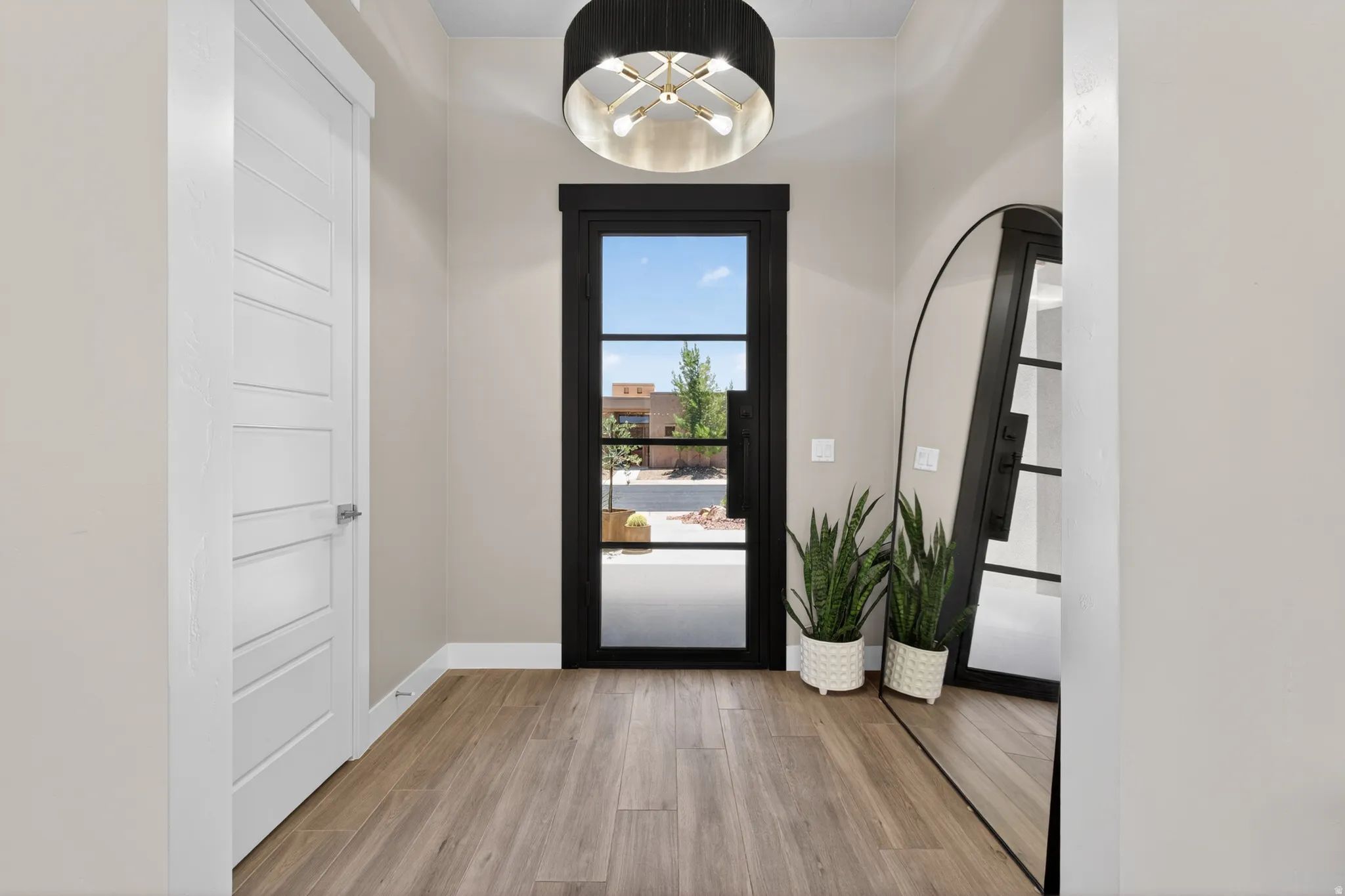 Entryway featuring a black-framed glass panel door, wood-finish flooring, a modern drum pendant light fixture, and light neutral wall tones