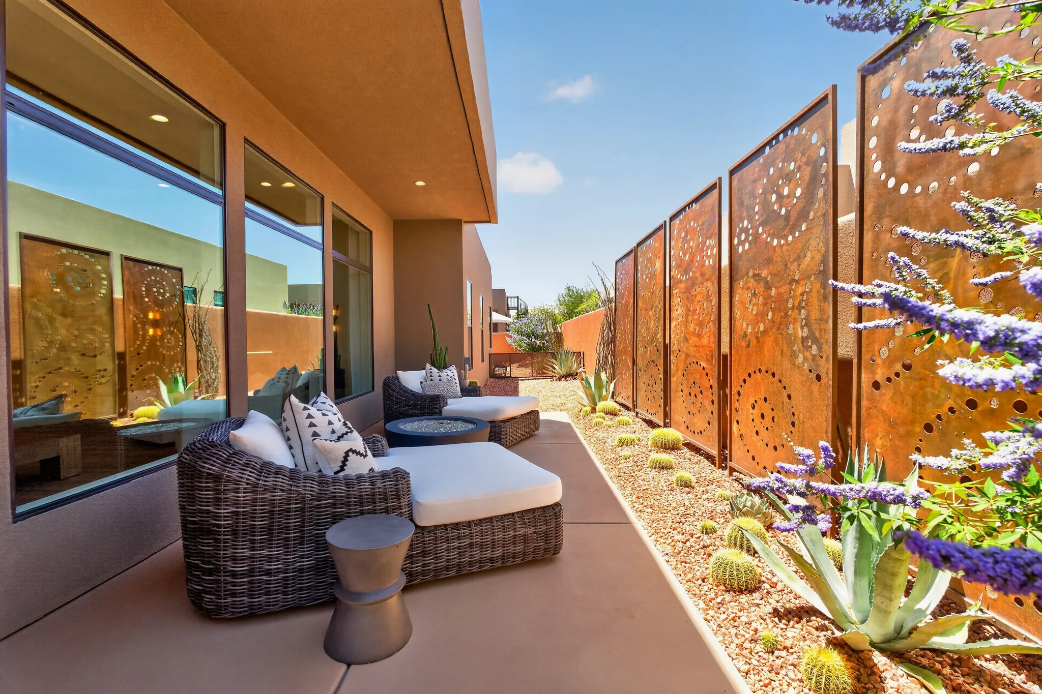 Expansive exterior patio #2 featuring a concrete surface, a decorative metal screen wall, a gravel xeriscape with cacti and succulents, and large picture windows