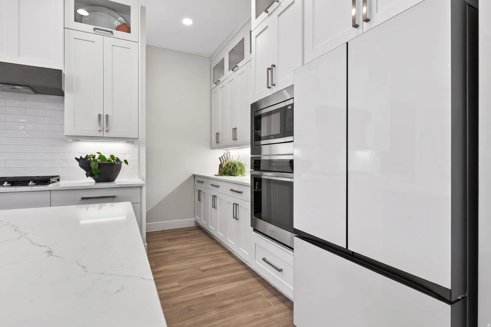 Modern kitchen featuring white cabinetry, quartz countertops, stainless steel appliances, wood-finish flooring, and subway tile backsplash