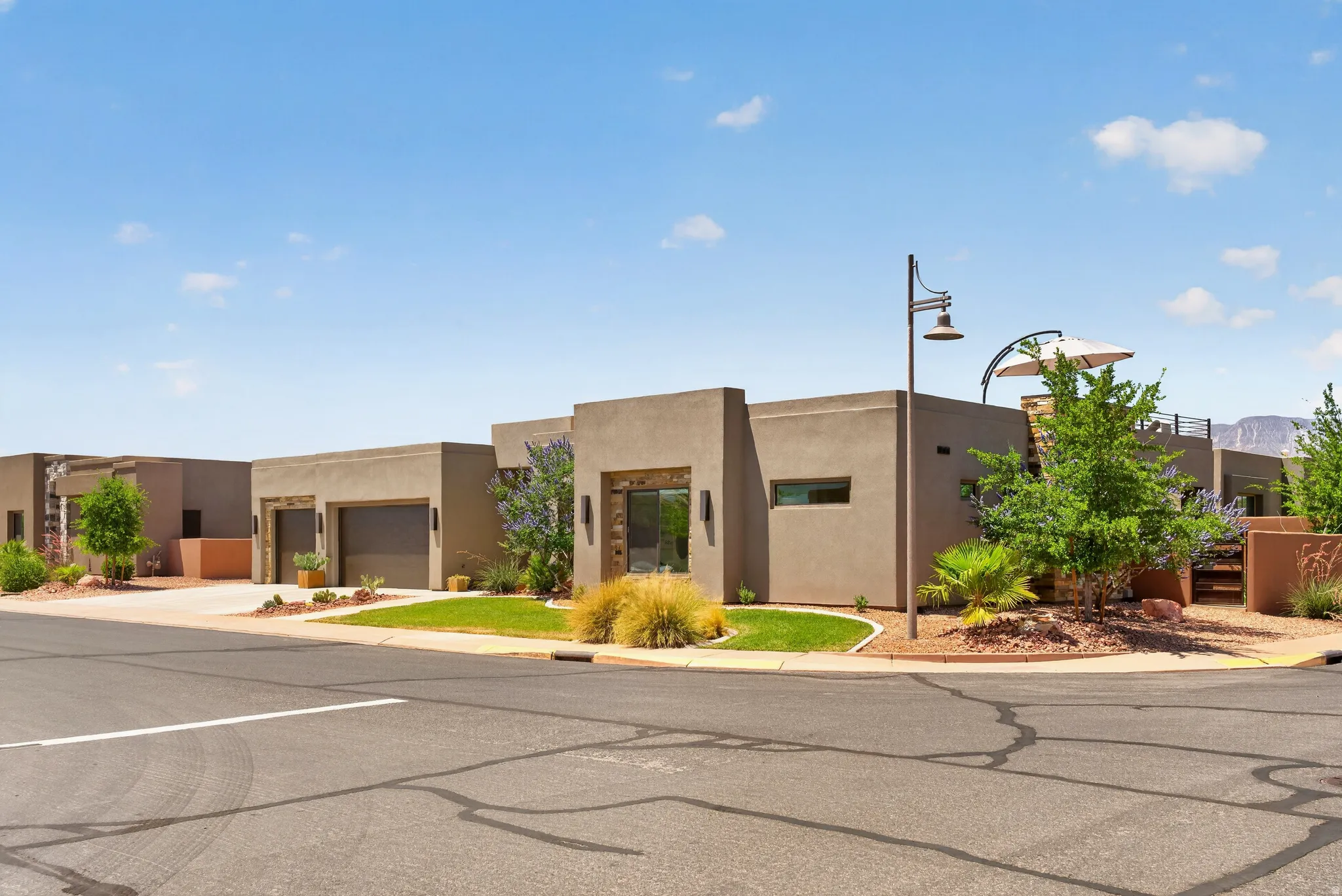 Modern stucco exterior with flat rooflines, integrated two-car garage, established desert landscaping, and a street-facing entryway
