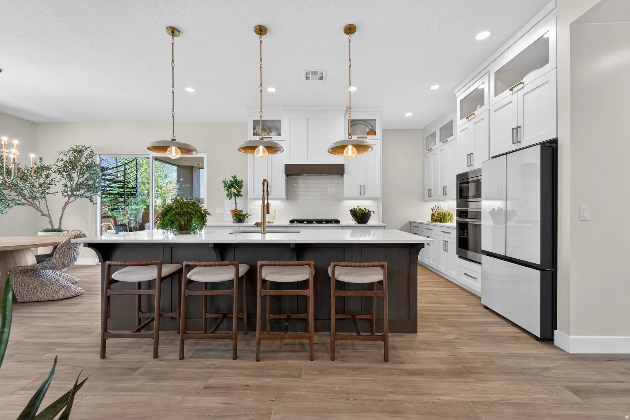 Contemporary kitchen featuring a dark wood island with white countertop, white cabinetry with glass-front uppers, and stainless steel appliances