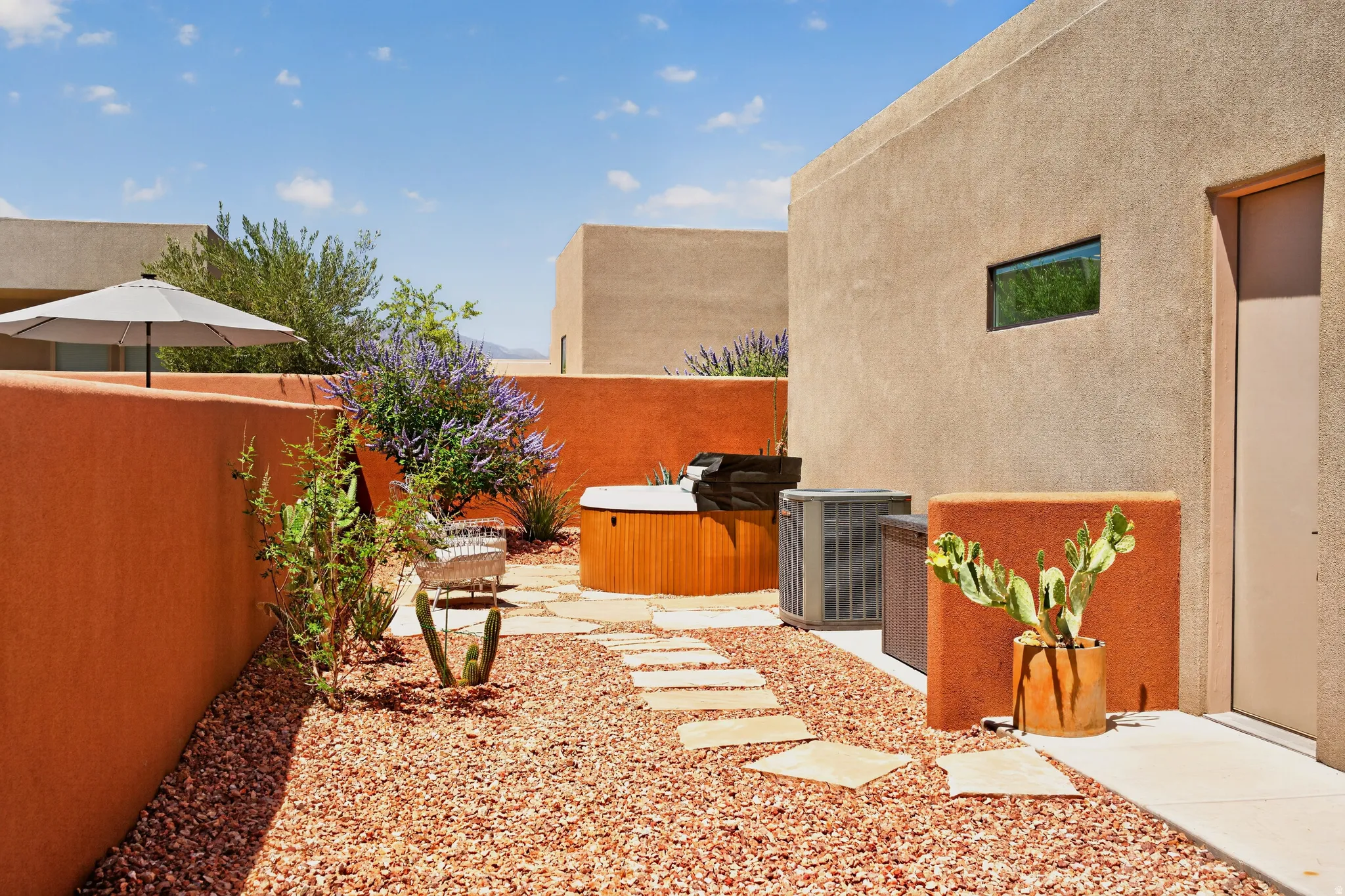 Private courtyard featuring a wood-panel hot tub, stepping stone pathway, arid landscaping, and surrounding stucco walls