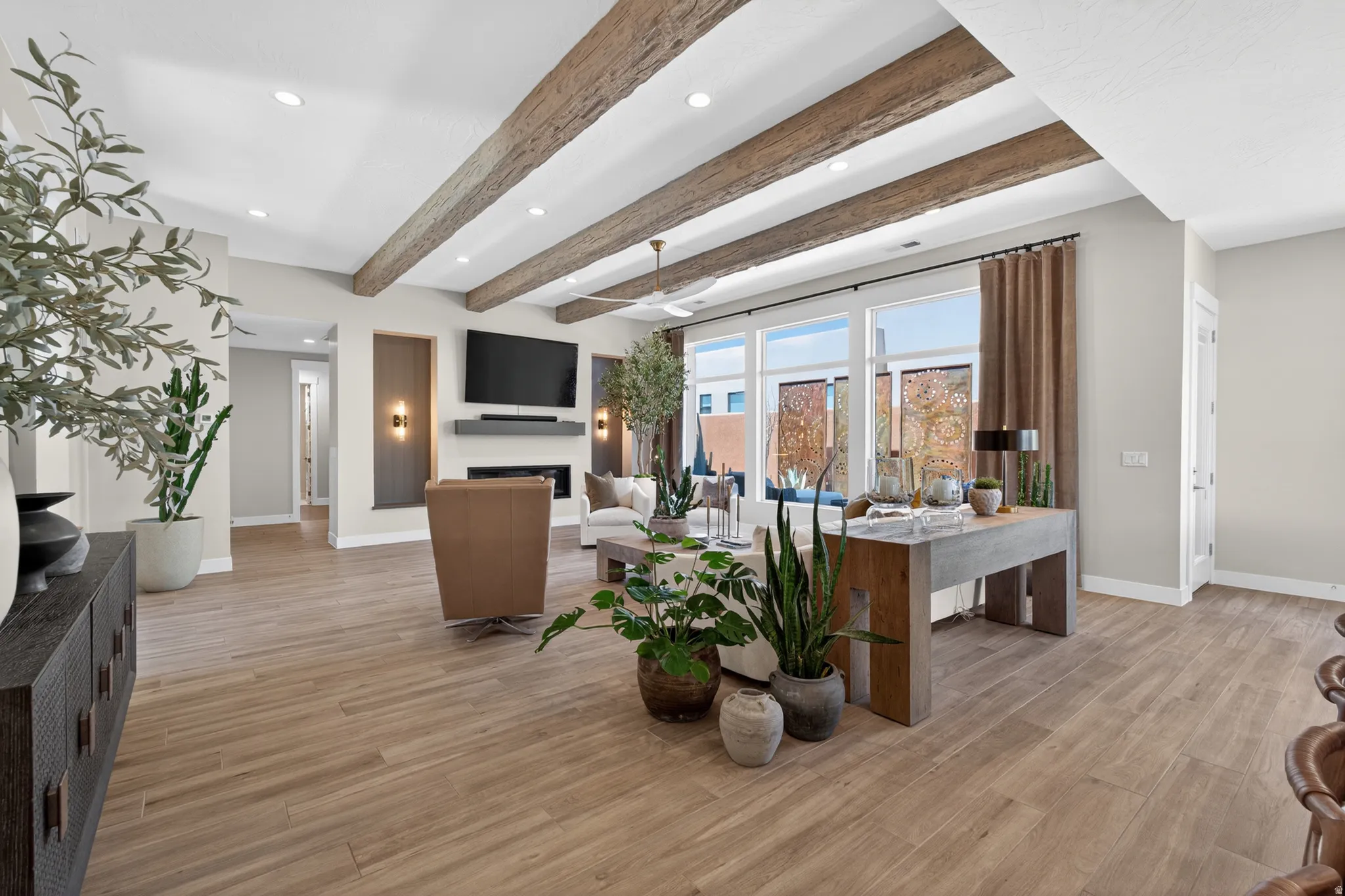 Spacious living area featuring wood-finish flooring, exposed ceiling beams, recessed lighting, and a modern fireplace with integrated shelving