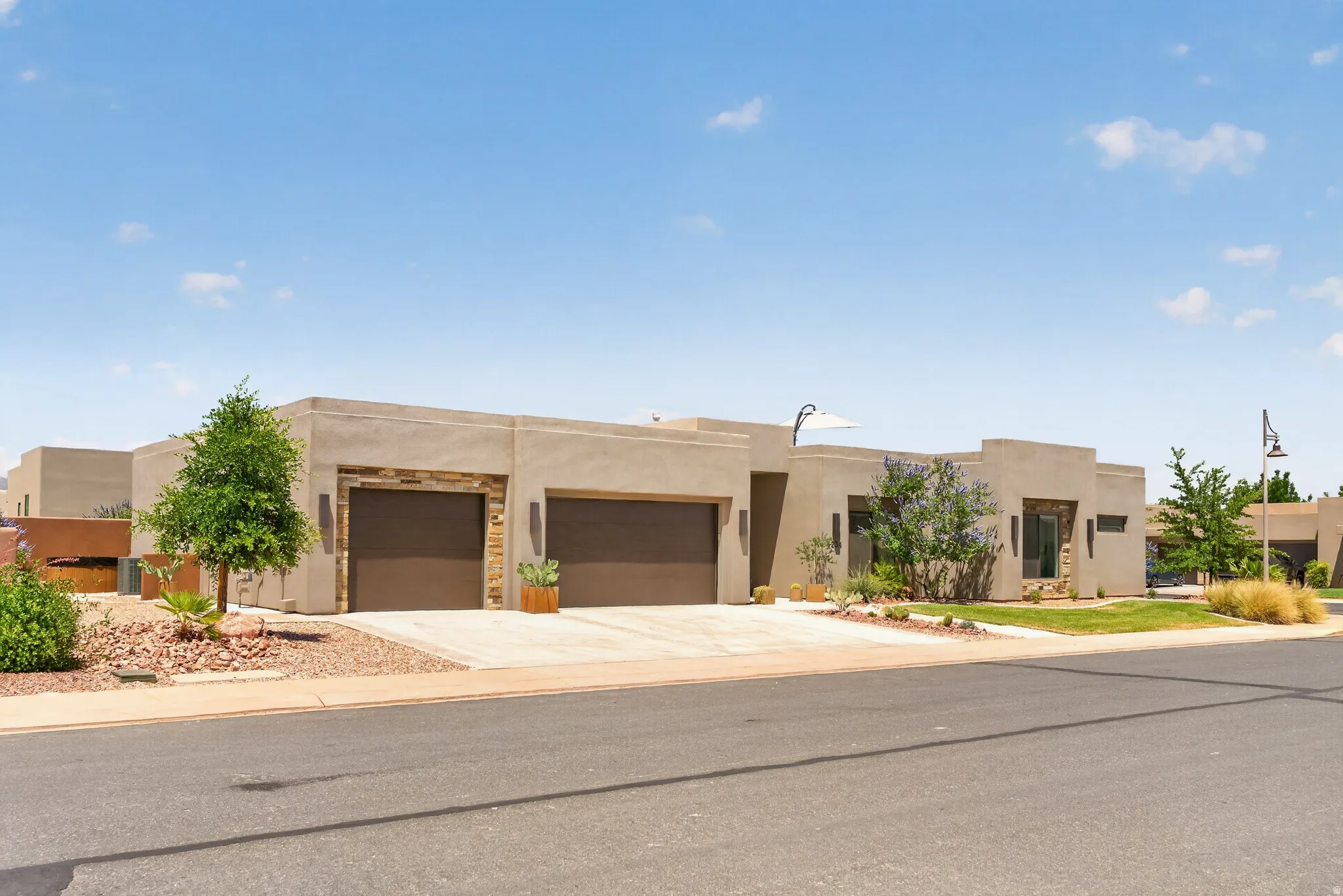 Contemporary stucco exterior featuring stone accents, dual garage doors, and xeriscaped landscaping