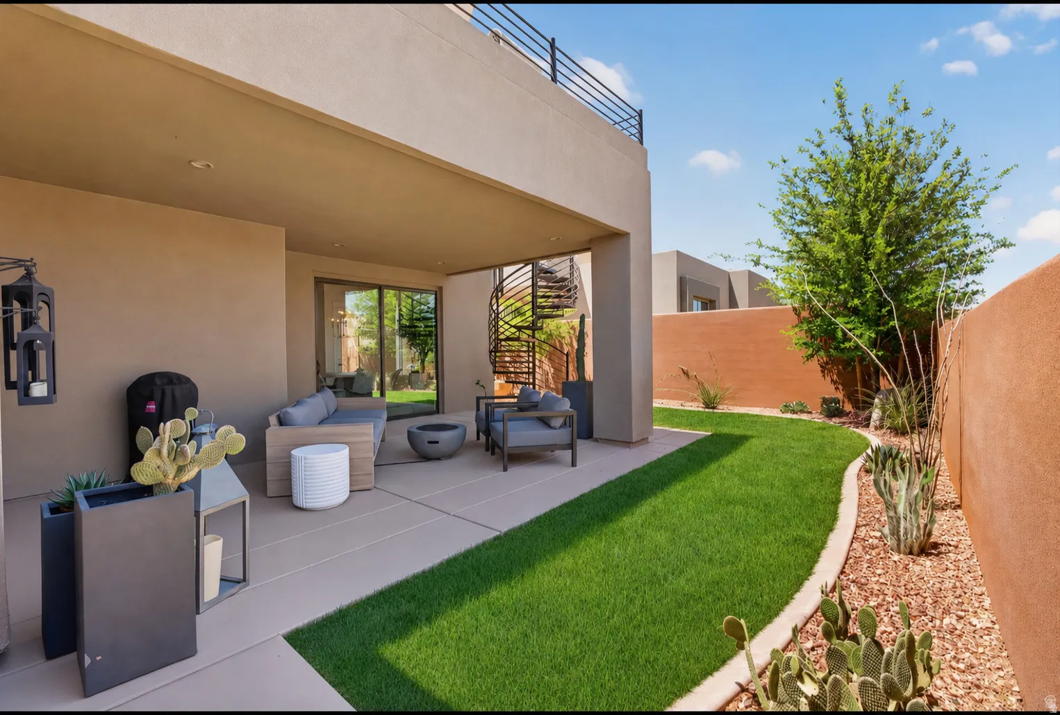 Expansive outdoor living area featuring a covered patio, spiral staircase to an upper balcony, and a manicured lawn