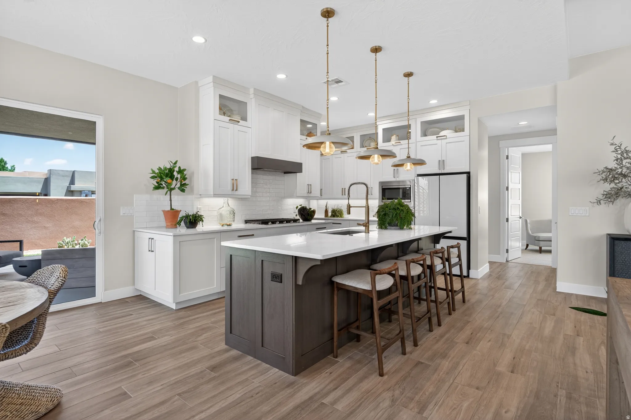 Spacious open-concept kitchen featuring a large central island with seating, white shaker cabinetry, wood-finish flooring, and direct access to an outdoor patio