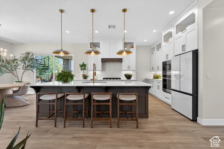 Contemporary kitchen featuring a dark wood island with white countertop, white cabinetry with glass-front uppers, and stainless steel appliances