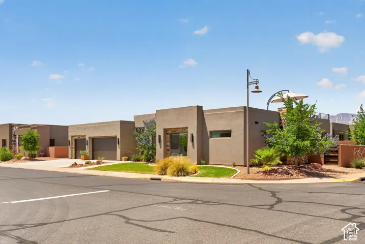 Modern stucco exterior with flat rooflines, integrated two-car garage, established desert landscaping, and a street-facing entryway