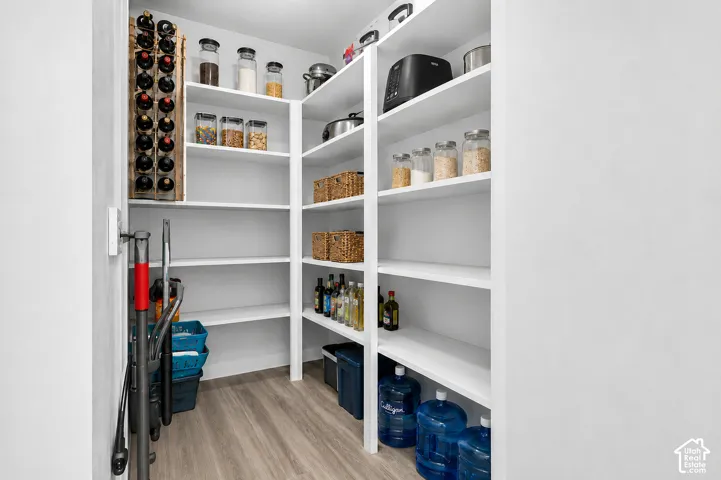 Spacious walk-in pantry featuring extensive built-in shelving, wood-finish flooring, and a dedicated wine rack