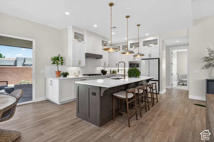 Spacious open-concept kitchen featuring a large central island with seating, white shaker cabinetry, wood-finish flooring, and direct access to an outdoor patio