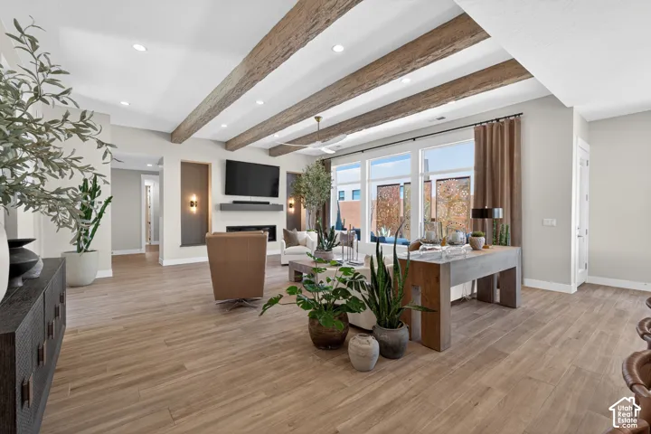 Spacious living area featuring wood-finish flooring, exposed ceiling beams, recessed lighting, and a modern fireplace with integrated shelving