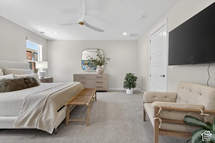 Spacious bedroom featuring light neutral wall tones, light gray carpeting, a large window with natural light, a modern ceiling fan, and a paneled interior door