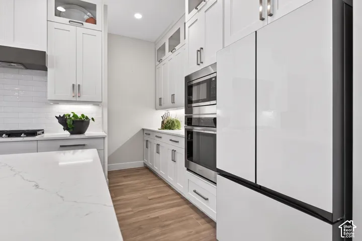 Modern kitchen featuring white cabinetry, quartz countertops, stainless steel appliances, wood-finish flooring, and subway tile backsplash