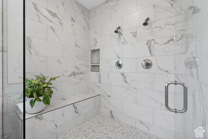 Spacious walk-in shower featuring large format tile walls, a built-in bench, and a mosaic tile floor