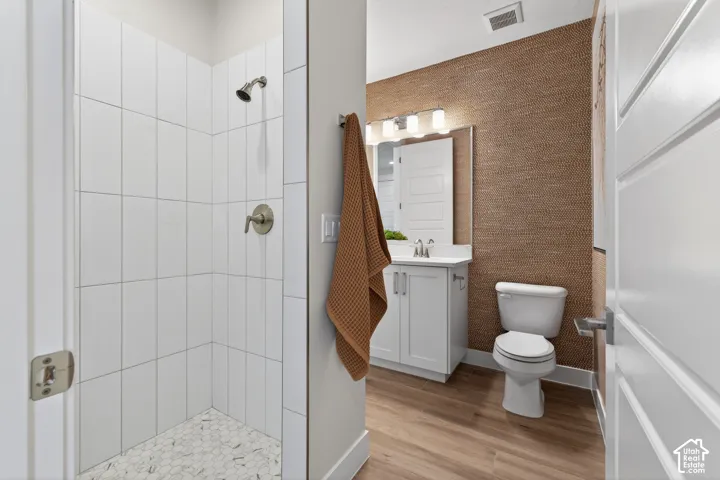 Bathroom featuring a walk-in shower with vertical subway tile, hexagon tile flooring, a single vanity with a white countertop, wood-finish flooring, and textured wall covering