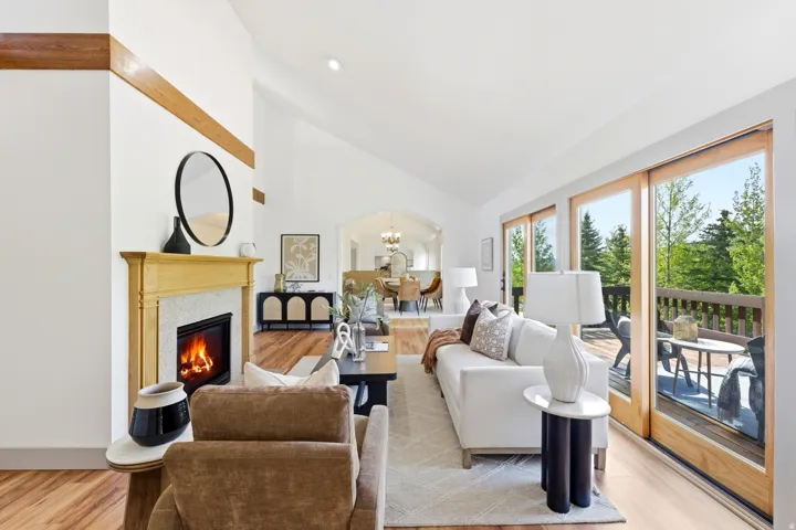 Vaulted ceiling living area featuring a fireplace with a light wood mantel, stone surround, and wood-finish flooring