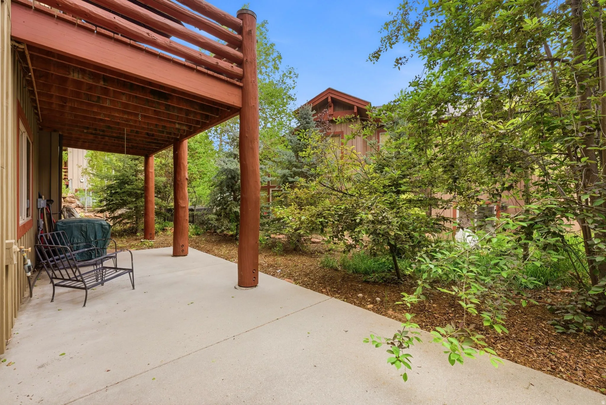 Ground-level patio with overhead deck featuring log-style railings, supported by log columns