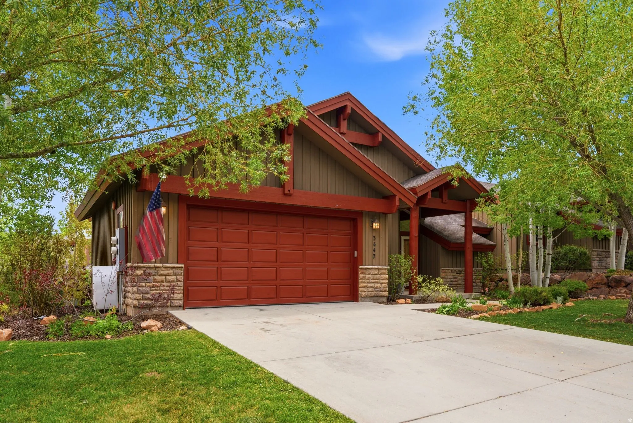 Craftsman-style exterior with a deep red garage door, stone accents, a covered entry, and a concrete driveway