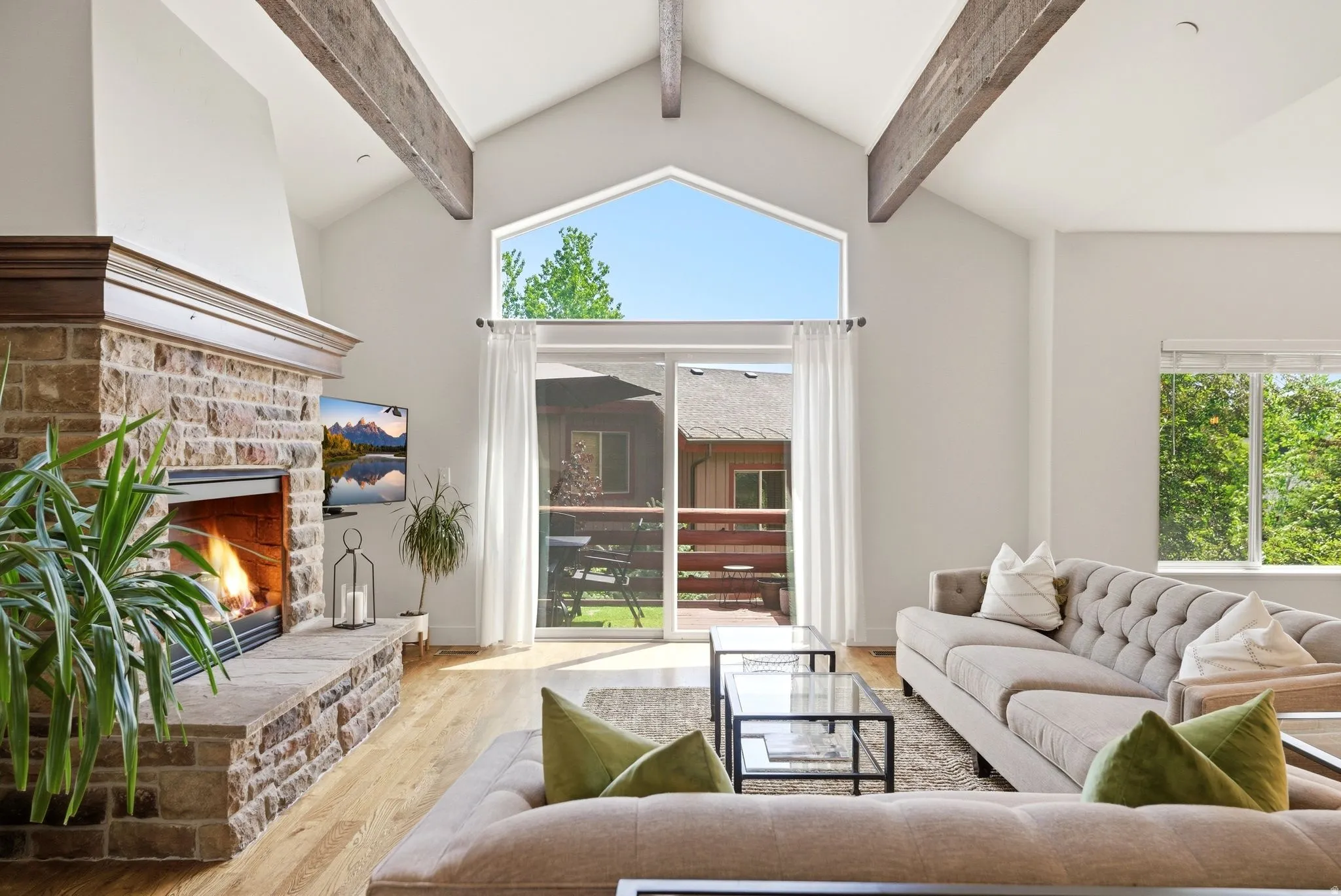 Great room featuring a stone-clad fireplace with a wood mantel, vaulted ceilings with exposed wood beams, and wood-finish flooring