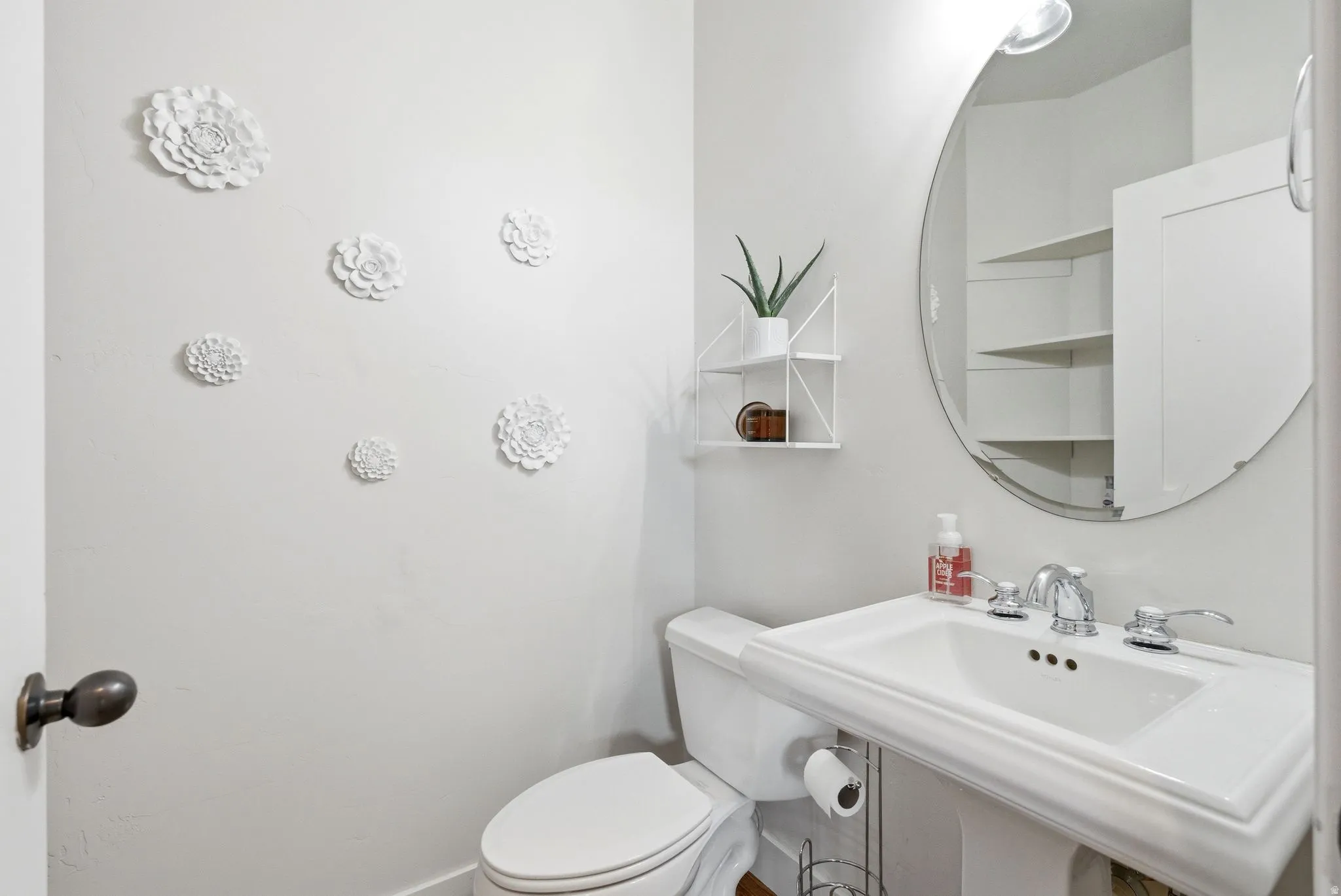 Pedestal sink with chrome fixtures and a circular wall mirror