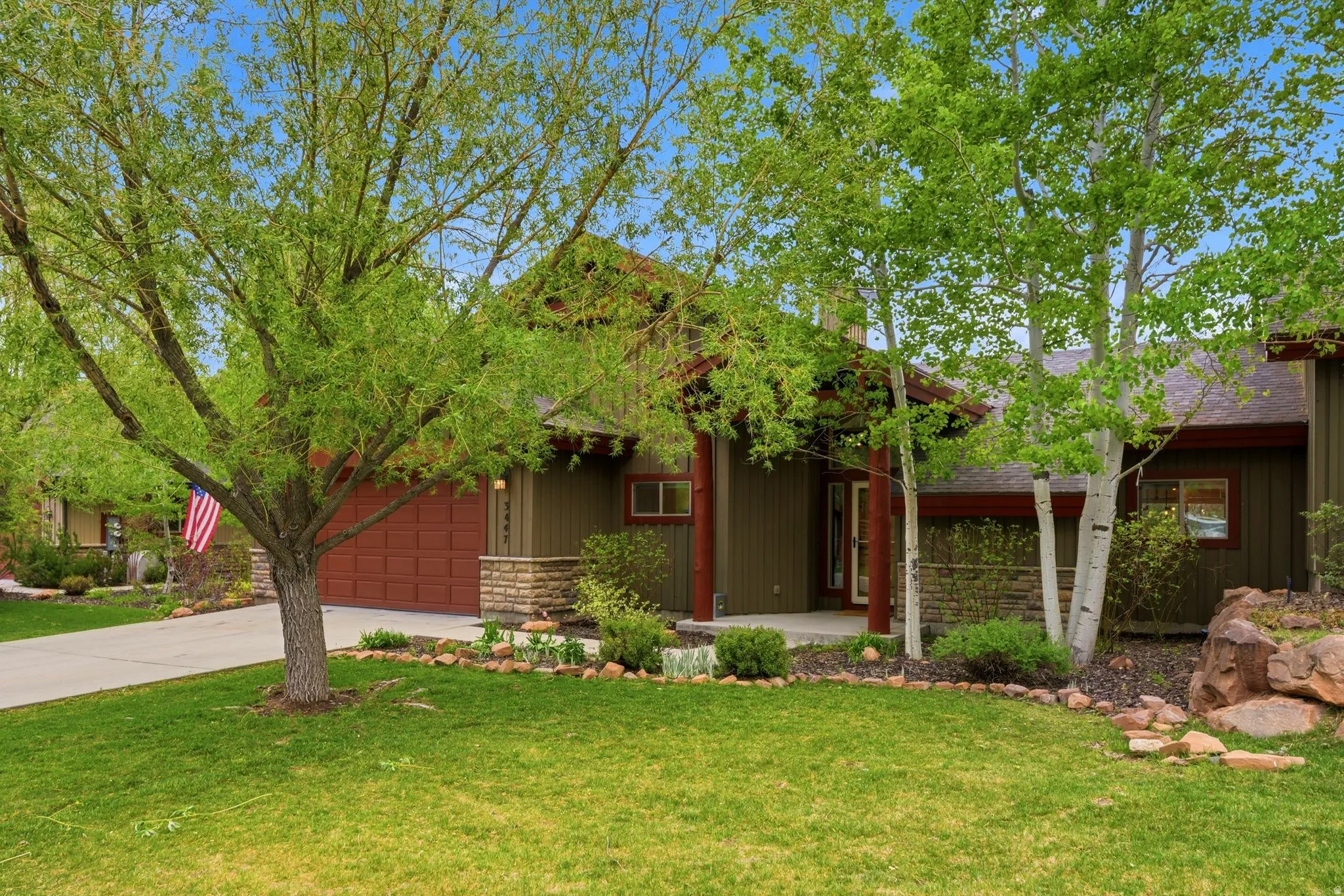 Exterior featuring green siding, a red garage door, and a stone accent facade