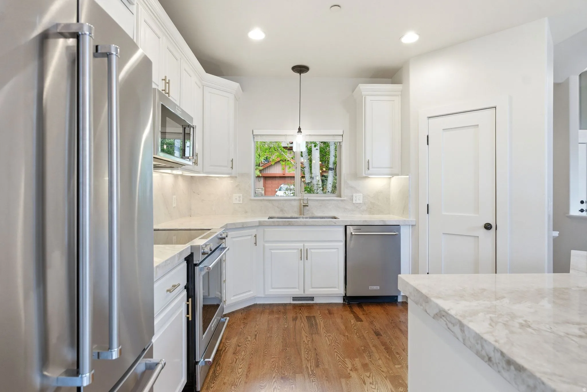 Kitchen featuring white cabinetry, stainless steel appliances, light-toned countertops, wood-finish flooring, and recessed lighting