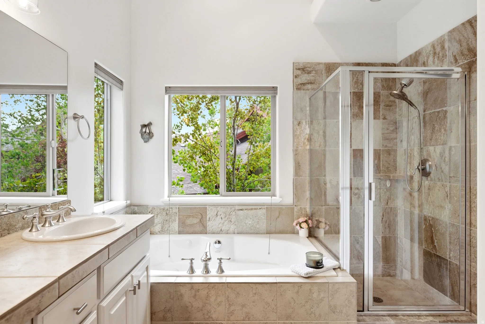 Bathroom featuring a built-in soaking tub, a separate glass-enclosed shower, a vanity with an undermount sink and tile countertop, and multiple windows