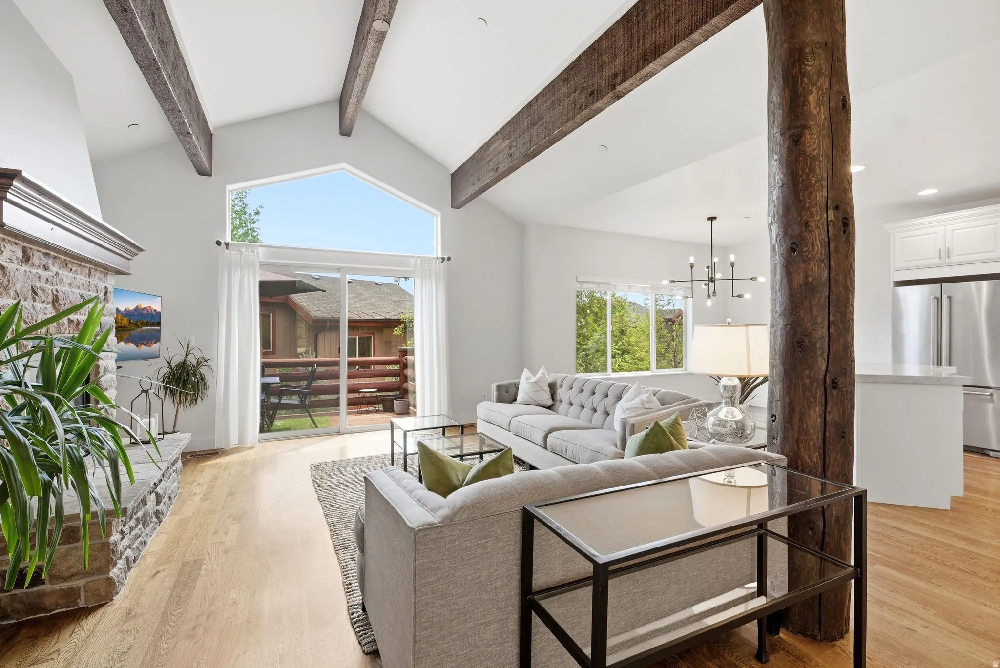 Living area featuring a vaulted ceiling with exposed wood beams, a stone fireplace, and wood-finish flooring