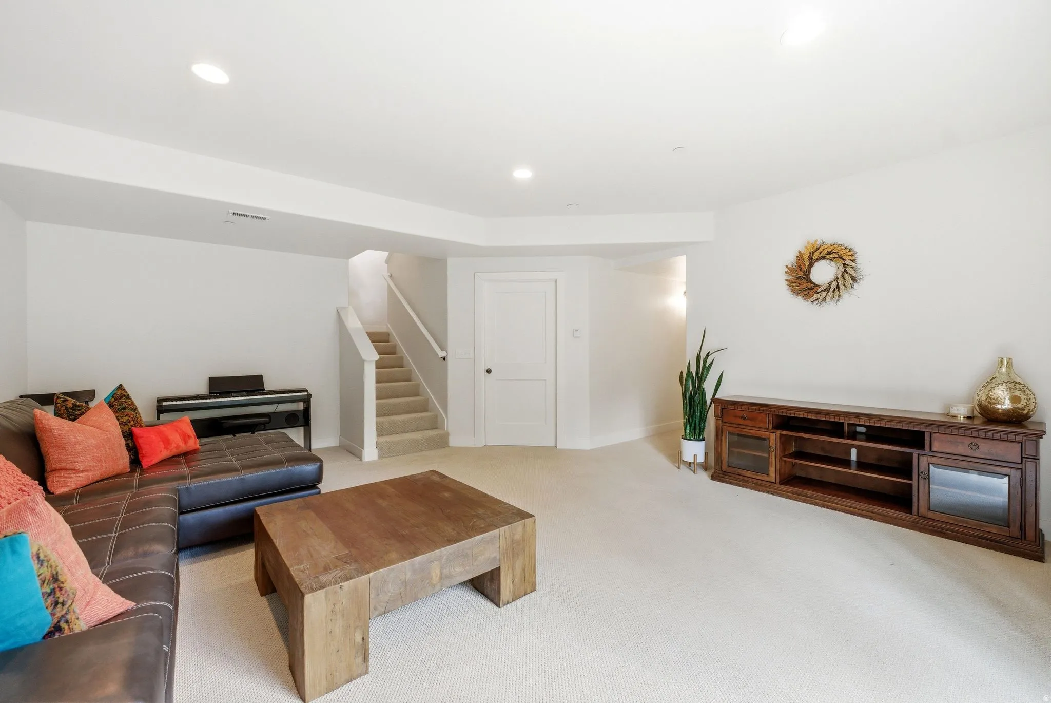 Spacious lower-level area with recessed lighting, light-colored carpet flooring, a white paneled door, and a staircase with a white railing