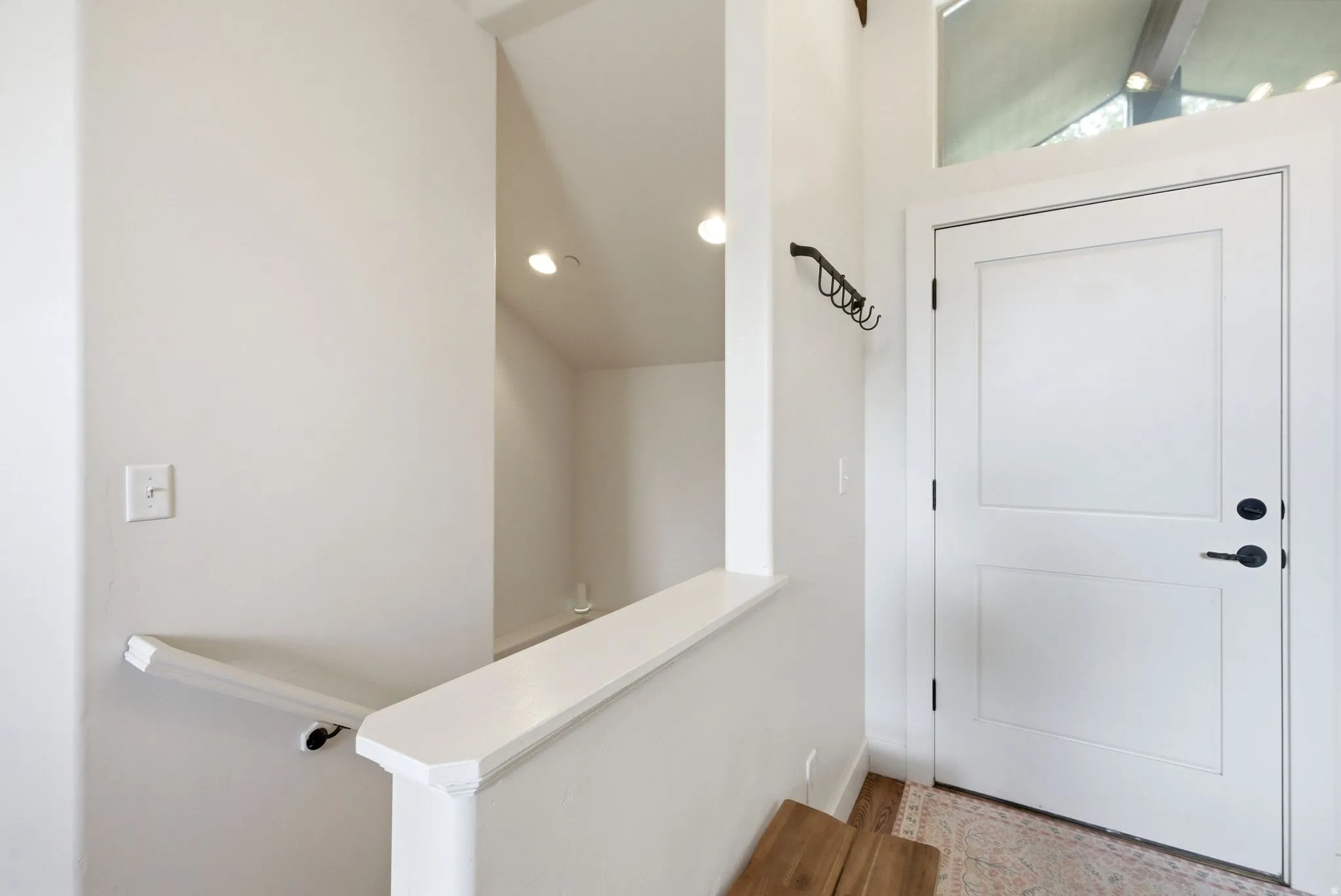 Entryway featuring a white paneled door with black hardware, an upper transom window, and a built-in coat rack