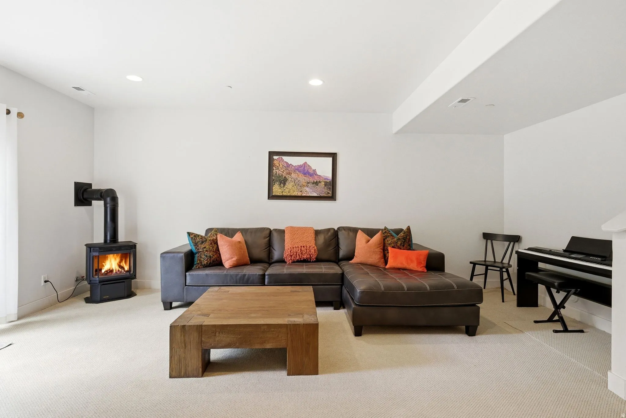 Living area featuring a freestanding wood-burning stove with black piping, white walls, recessed ceiling lighting, and light-colored carpet flooring