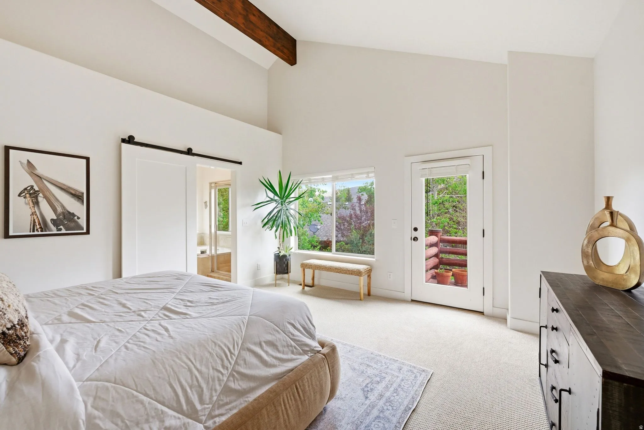 Vaulted ceiling featuring an exposed wood beam, a white barn door, expansive windows, a glass-paned door, and light-toned carpeting
