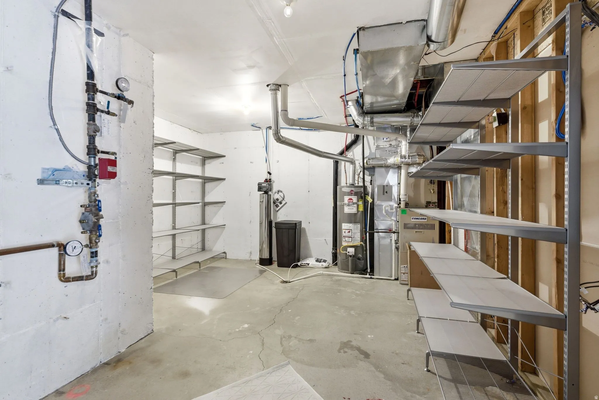 Concrete floor basement space featuring extensive built-in shelving, visible HVAC system, water heater, and water softener