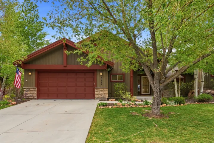 Craftsman-style exterior featuring a striking green and red color palette, stone accents, a two-car garage, mature landscaping, and a concrete driveway